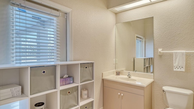 bathroom featuring vanity, toilet, a healthy amount of sunlight, and a textured wall