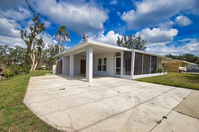 back of property with a carport, concrete driveway, a yard, and a sunroom