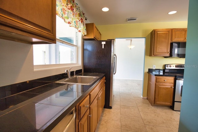 kitchen with stainless steel appliances, dark countertops, visible vents, brown cabinetry, and a sink