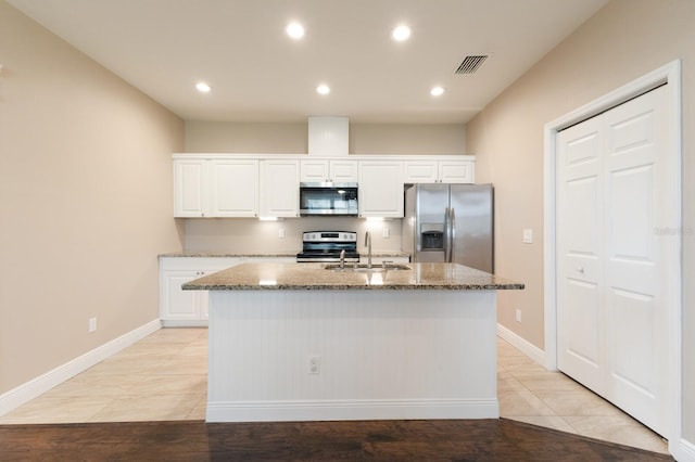 kitchen with stone countertops, stainless steel appliances, visible vents, white cabinets, and a center island with sink