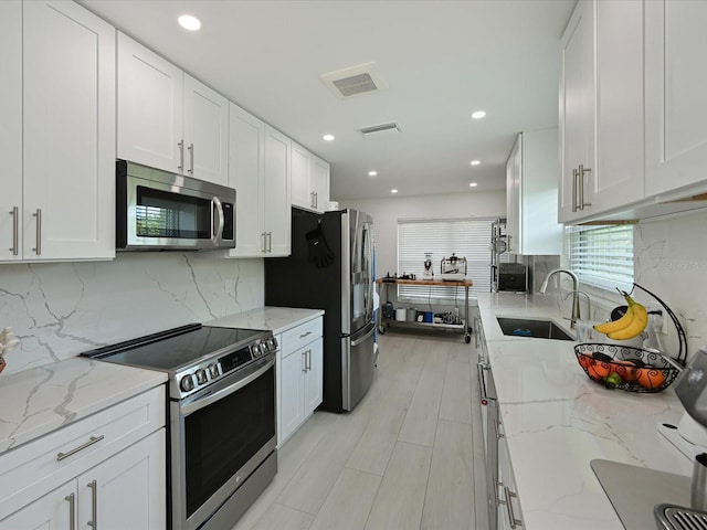 kitchen with appliances with stainless steel finishes, white cabinetry, a sink, and visible vents