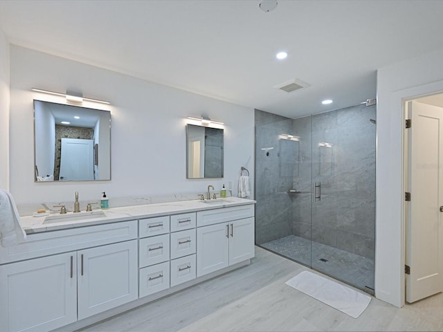 bathroom with double vanity, wood finished floors, a sink, and a shower stall