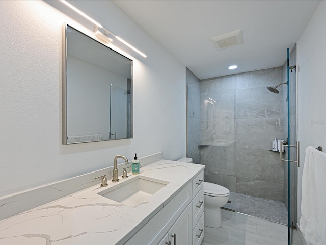 bathroom featuring visible vents, tiled shower, vanity, and toilet