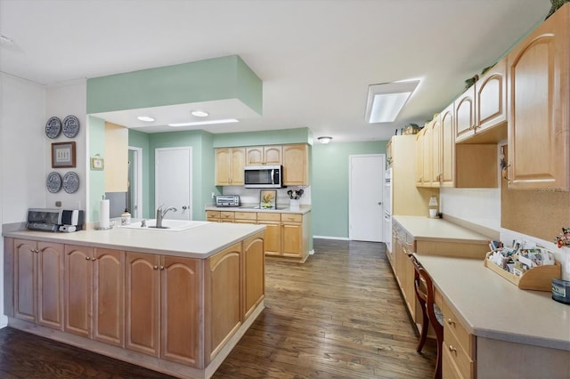 kitchen featuring light brown cabinets, a sink, stainless steel microwave, a peninsula, and dark wood-style flooring