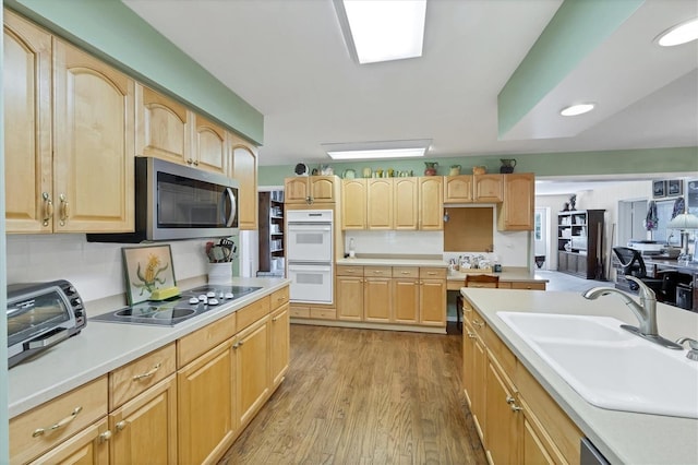 kitchen with stainless steel microwave, light brown cabinets, black electric stovetop, double oven, and a sink