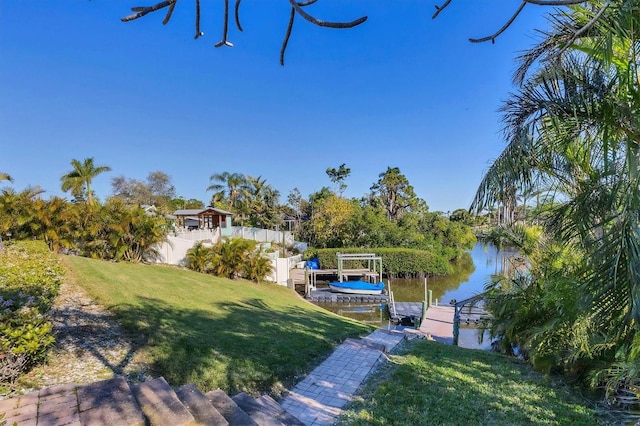 view of yard with boat lift, fence, a dock, and a water view