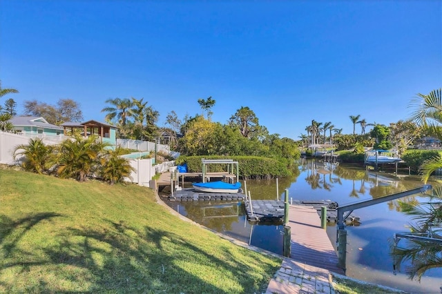 dock area featuring a water view, boat lift, a lawn, and fence