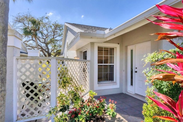 entrance to property with a shingled roof, fence, and stucco siding