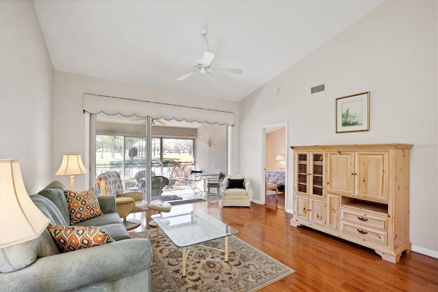 living area featuring baseboards, visible vents, a ceiling fan, light wood-style floors, and high vaulted ceiling