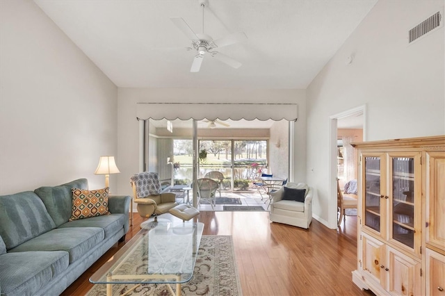 living area featuring ceiling fan, wood finished floors, visible vents, baseboards, and vaulted ceiling