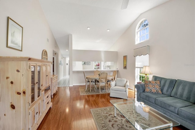 living room featuring high vaulted ceiling, light wood finished floors, and baseboards