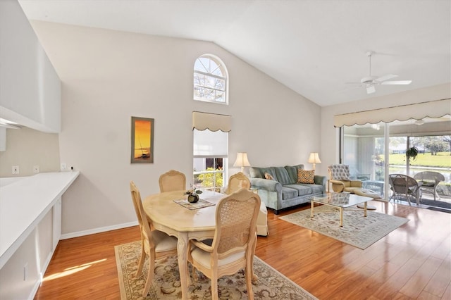 dining space featuring baseboards, high vaulted ceiling, light wood-style flooring, and a ceiling fan