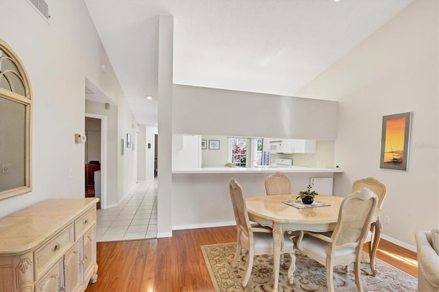 dining space with baseboards, vaulted ceiling, and light wood finished floors