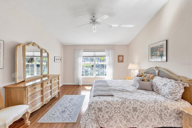 bedroom with baseboards, ceiling fan, wood finished floors, vaulted ceiling, and a textured ceiling