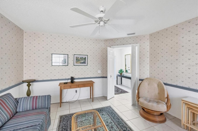 sitting room featuring a ceiling fan, tile patterned floors, visible vents, and wallpapered walls