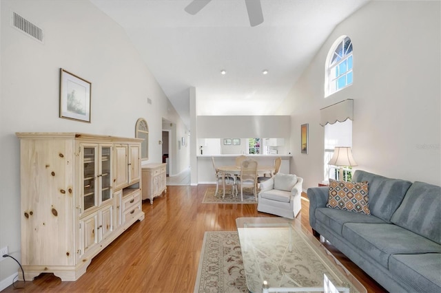 living room featuring high vaulted ceiling, light wood-type flooring, visible vents, and baseboards