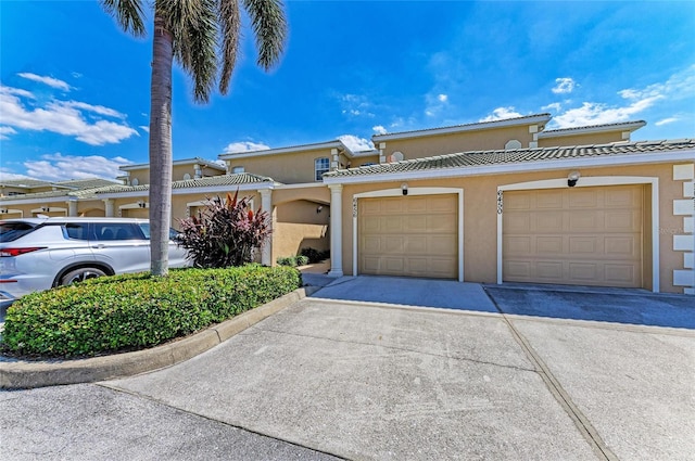 view of property featuring driveway, a tile roof, a garage, and stucco siding