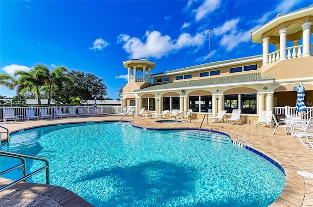 pool with a patio area, fence, and a hot tub