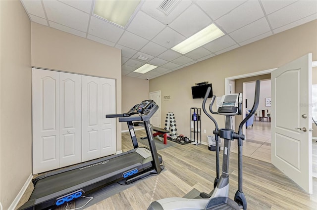 exercise area with a paneled ceiling, light wood-style flooring, visible vents, and baseboards