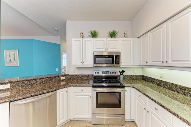 kitchen with light tile patterned floors, appliances with stainless steel finishes, white cabinets, and dark stone countertops