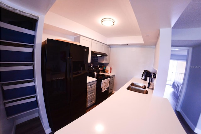 kitchen with black appliances, a sink, under cabinet range hood, tasteful backsplash, and light countertops