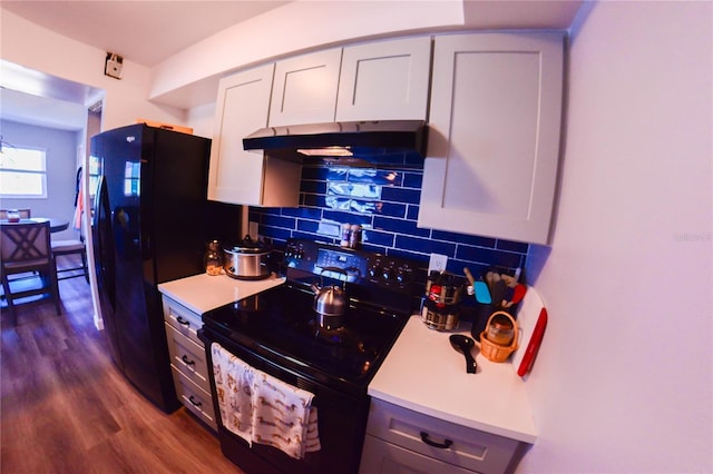 kitchen with under cabinet range hood, light countertops, decorative backsplash, black appliances, and dark wood-style flooring