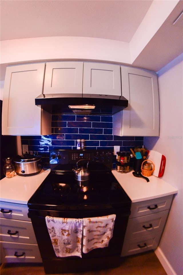 kitchen with under cabinet range hood, black electric range, light countertops, and backsplash