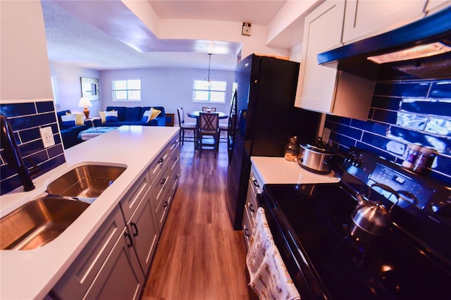 kitchen with black range with electric stovetop, under cabinet range hood, dark wood-style floors, light countertops, and decorative backsplash