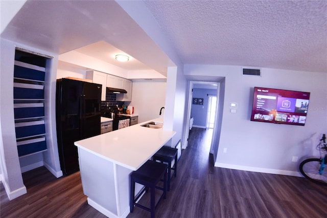 kitchen with visible vents, a kitchen bar, dark wood-type flooring, black appliances, and a sink