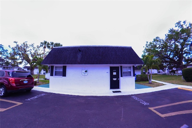 view of front of home featuring stucco siding, roof with shingles, and uncovered parking