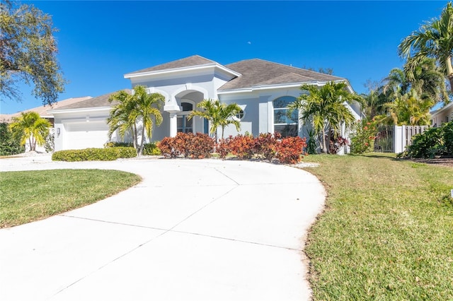 mediterranean / spanish-style house with concrete driveway, an attached garage, fence, a front yard, and stucco siding