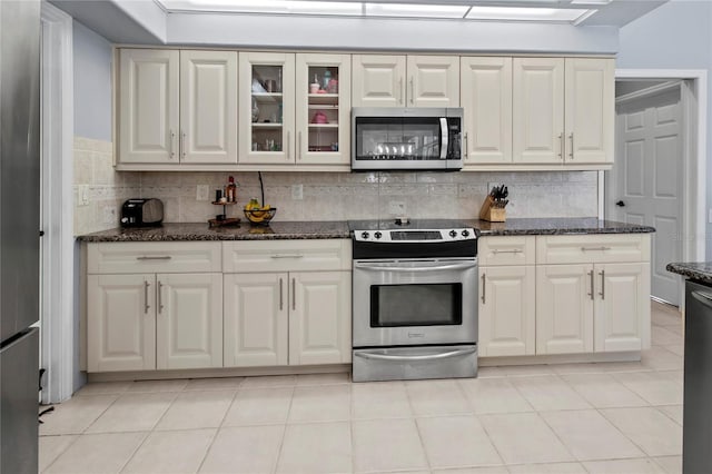 kitchen featuring light tile patterned floors, tasteful backsplash, dark stone counters, glass insert cabinets, and stainless steel appliances