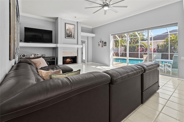 living room with a warm lit fireplace, ceiling fan, light tile patterned flooring, baseboards, and crown molding