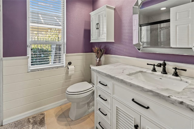 full bath with a stall shower, wainscoting, toilet, tile patterned flooring, and vanity