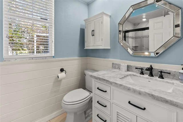 bathroom featuring a stall shower, wooden walls, wainscoting, toilet, and vanity