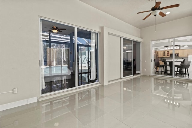 tiled spare room with a sunroom, a ceiling fan, and baseboards