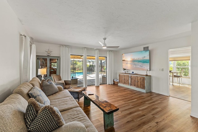 living area featuring ceiling fan, a textured ceiling, baseboards, and wood finished floors