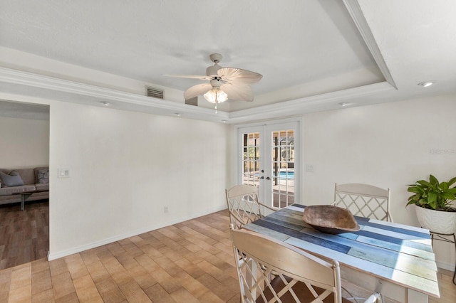 dining room featuring visible vents, baseboards, a tray ceiling, french doors, and light wood-style floors