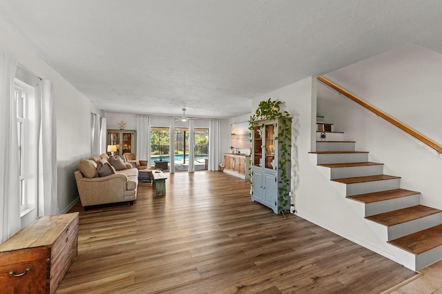 living area with stairs, a textured ceiling, baseboards, and wood finished floors