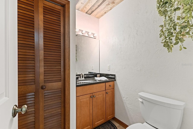 bathroom with a closet, a textured wall, vanity, and toilet