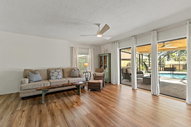 living room with a ceiling fan, a sunroom, light wood-style flooring, and a textured ceiling