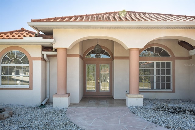 entrance to property with stucco siding, a tiled roof, and french doors