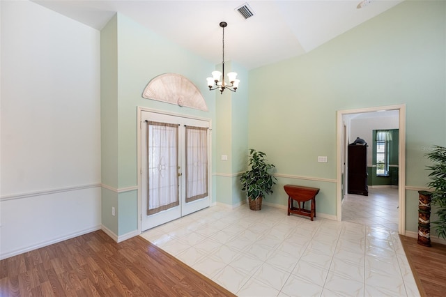 foyer entrance featuring light wood finished floors, visible vents, baseboards, french doors, and a notable chandelier