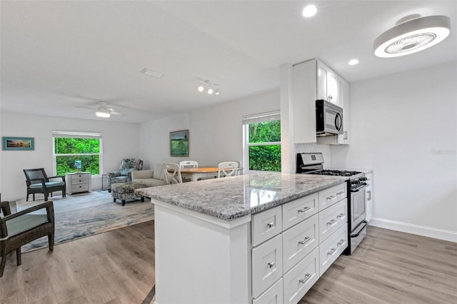 kitchen with light stone countertops, baseboards, light wood finished floors, stainless steel gas range, and white cabinets