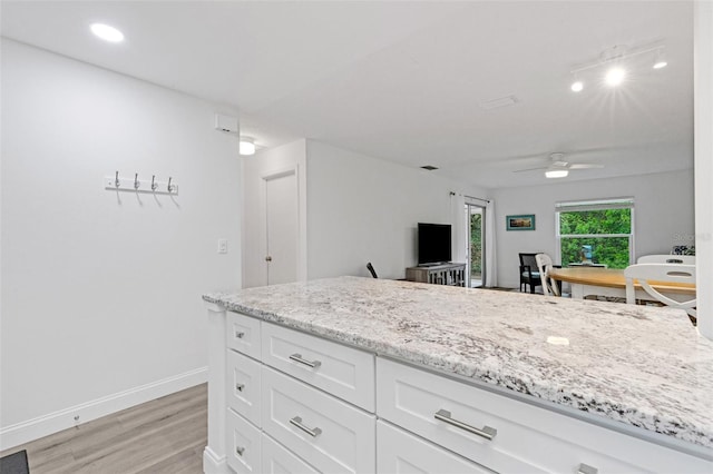 kitchen with light stone counters, a ceiling fan, baseboards, light wood finished floors, and white cabinetry