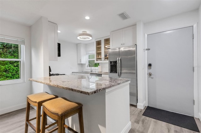 kitchen featuring visible vents, a kitchen bar, a sink, appliances with stainless steel finishes, and glass insert cabinets