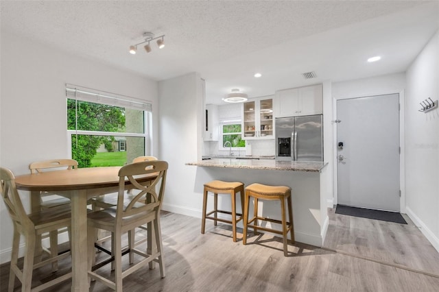 interior space featuring light wood-type flooring, visible vents, white cabinetry, stainless steel fridge with ice dispenser, and glass insert cabinets