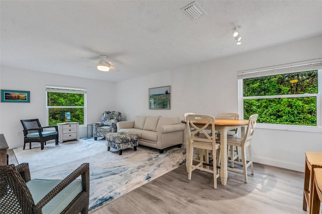 living area with wood finished floors, baseboards, visible vents, ceiling fan, and a textured ceiling