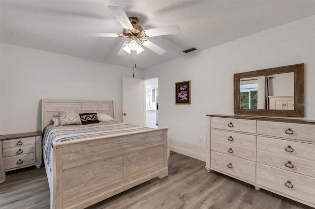 bedroom with visible vents, a ceiling fan, a textured ceiling, wood finished floors, and baseboards