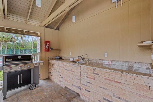 kitchen featuring a sink, wooden walls, light stone countertops, wood ceiling, and vaulted ceiling with beams